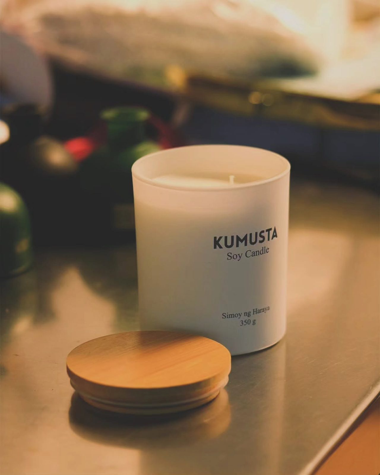 Cream-colored Kumusta candle with a wooden lid beside it on a table