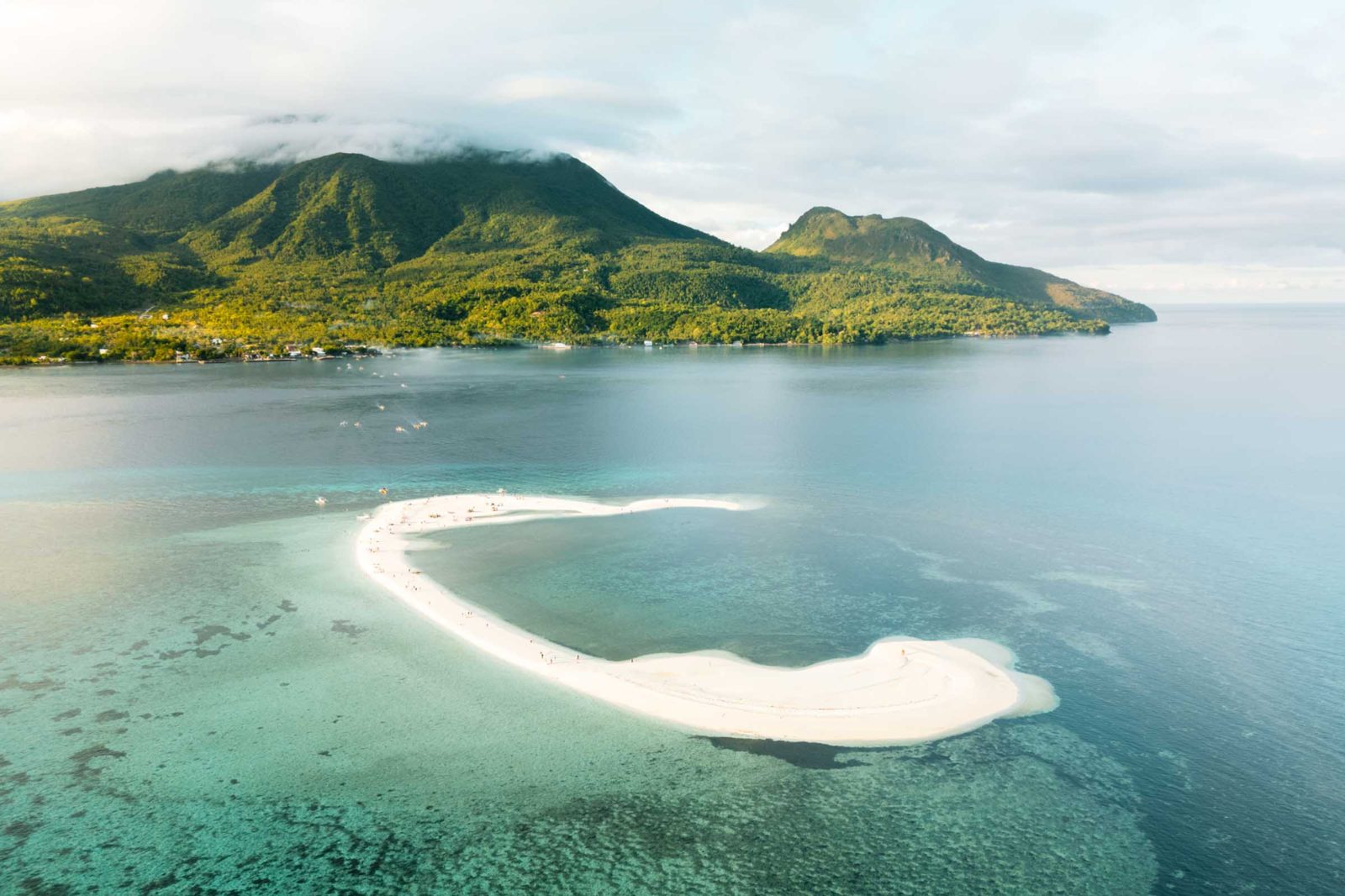 Curved White Island sandbar surrounded by clear water with Camiguin's green mountains behind it