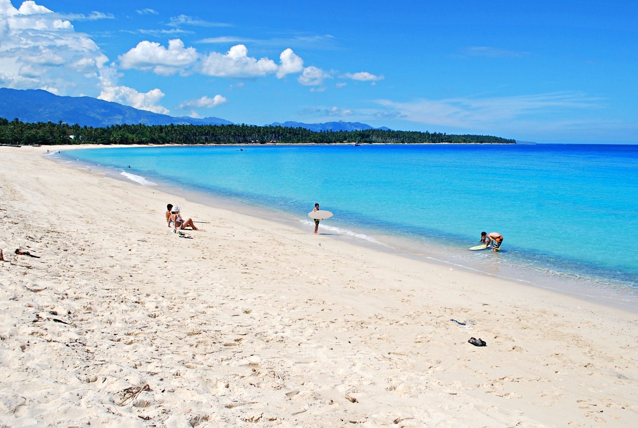 Visitors on a white-sand beach beside clear blue water near Davao